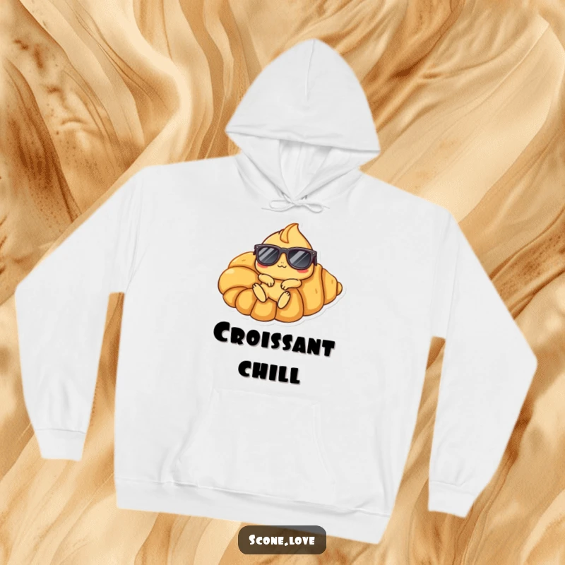 Funny Scone Croissant Hoodie: A scone character sporting sunglasses lounges on a giant croissant, showcasing ultimate relaxation.